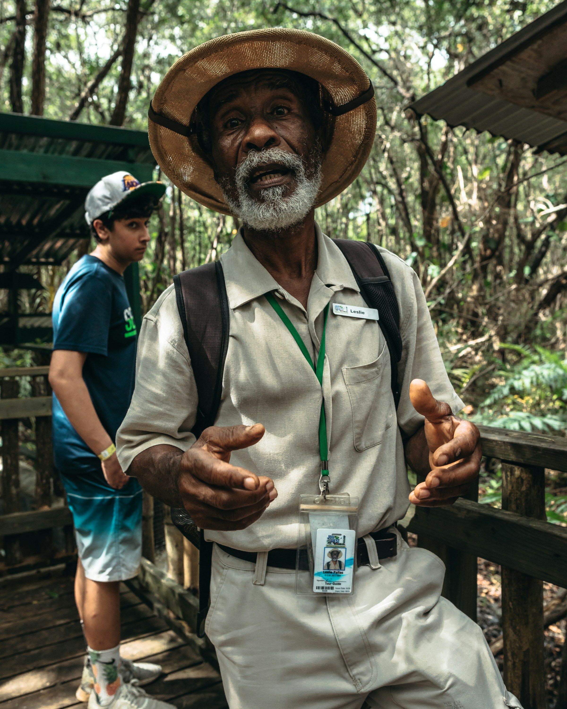 A tour guide in a sun hat talks to the group on a forest boardwalk